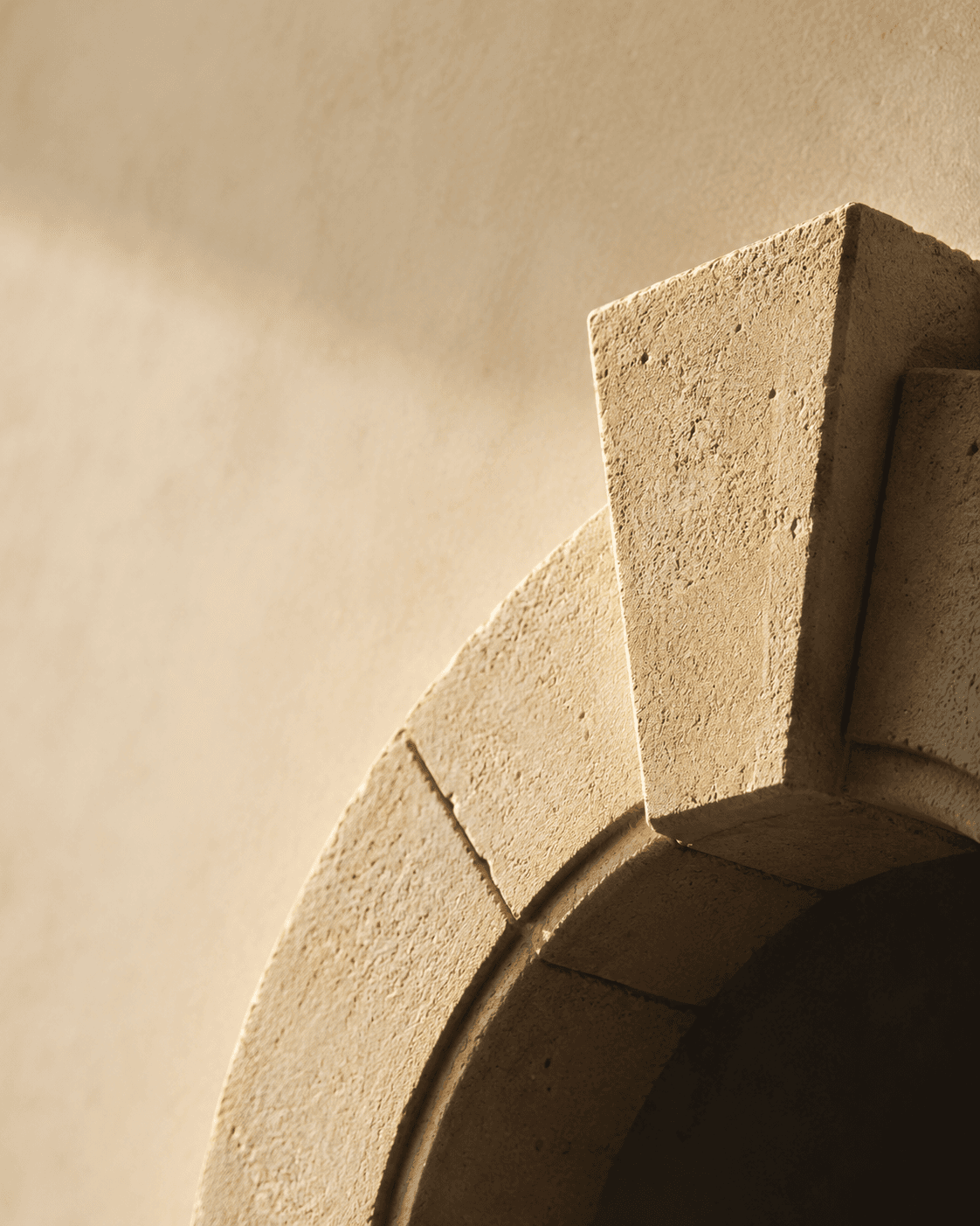 Warm light raking across a cream stone archway — keystone and voussoirs in sharp relief.